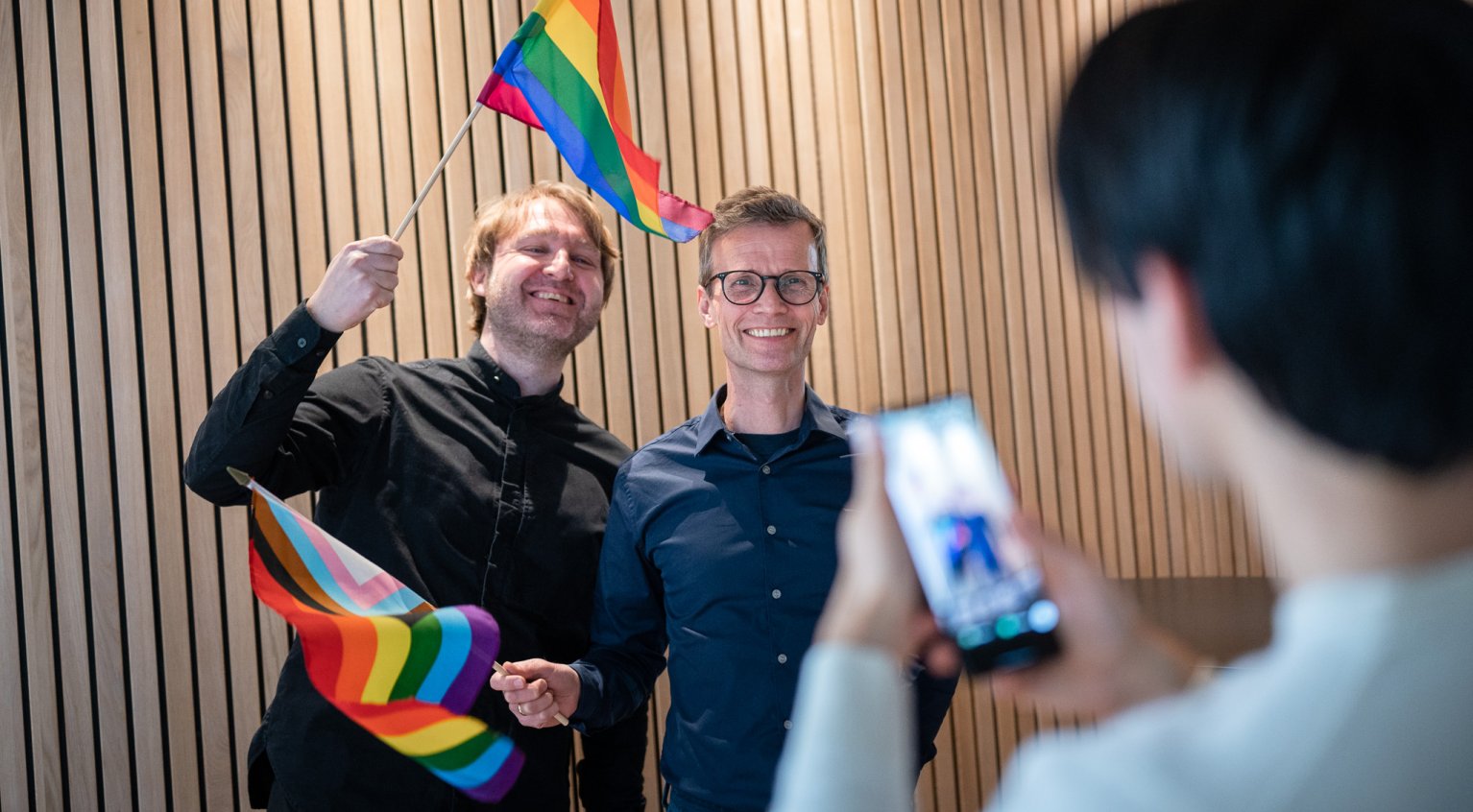 Portrett av Nils Petter Strømmen og Marius Jensen som vifter med regnbue-flagg.