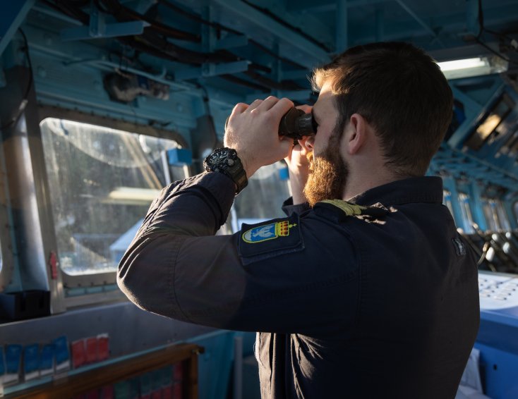 Illustrasjonsbilde til Forsvarets kurs i strategisk krisehåndtering. Bildet viser en kadett fra Sjøkrigsskolen som står inne i en båt og ser ut med kikkert.