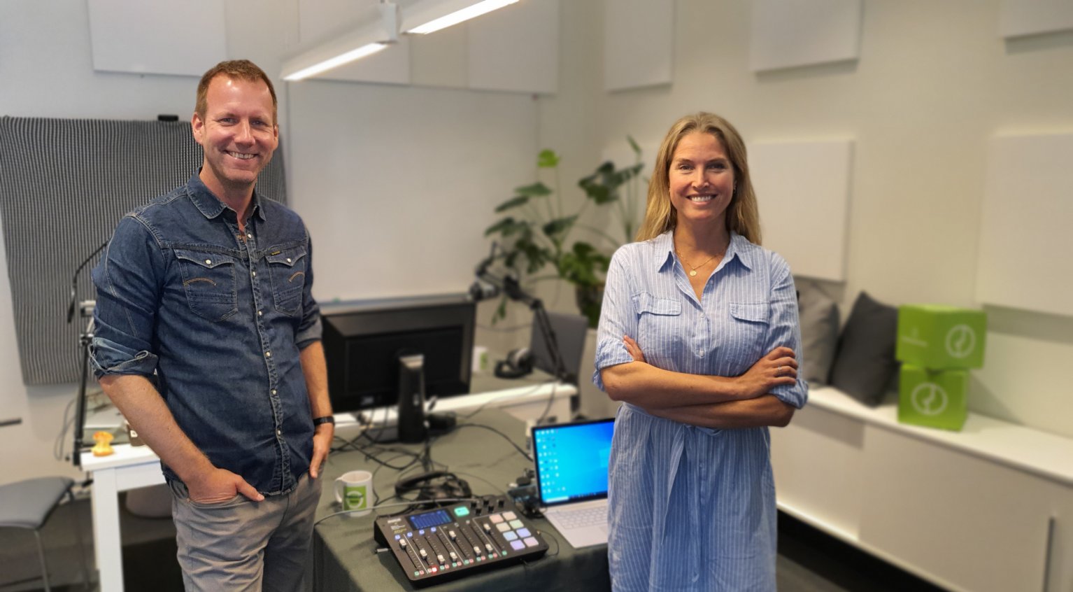 Eirik Bergesen (t.v) og Mari Mellum i podkast-studioet. I bakgrunnen ser du teknisk utstyr, begge to smiler til kamera.