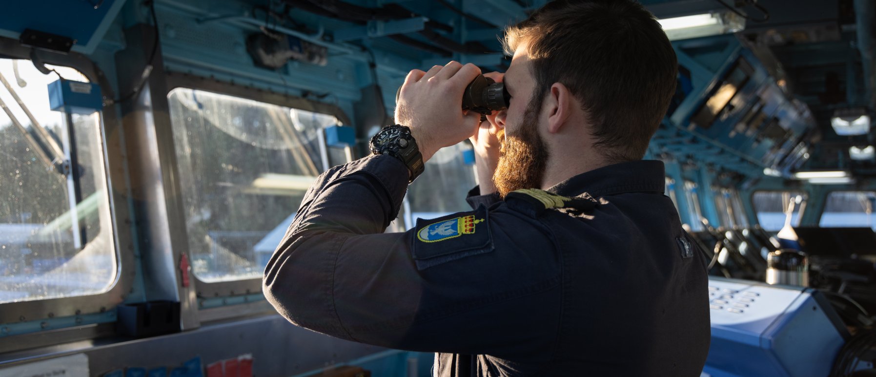 Illustrasjonsbilde til Forsvarets kurs i strategisk krisehåndtering. Bildet viser en kadett fra Sjøkrigsskolen som står inne i en båt og ser ut med kikkert.