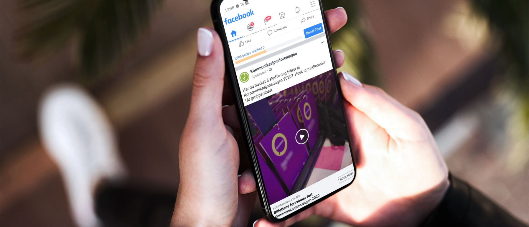 Nærbilde av en hånd som holder en mobil som viser en sponset post i Facebook appen.