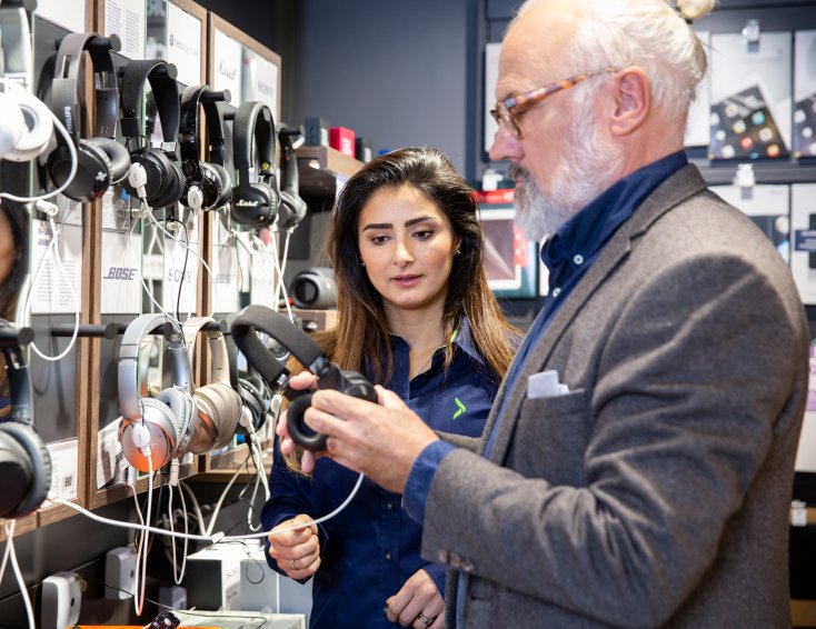 En Elgiganten ansatt hjelper en kunde med å velge headset.